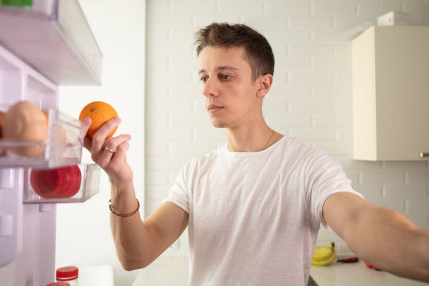 Kamera im Küchenschrank: Mann öffnet Kühlschranktür, schaut hinein. - Foto, Bild