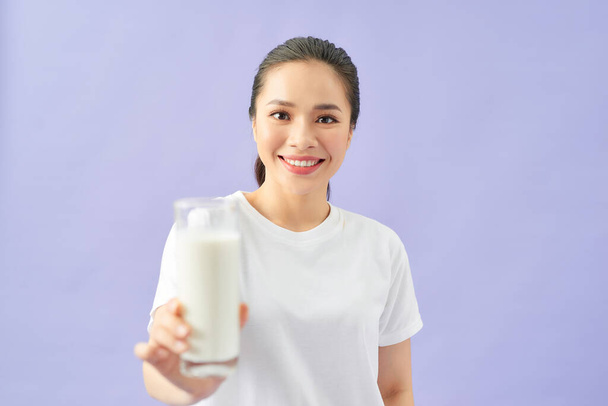 Schöne asiatische Frau zeigt ein Glas Milch, isoliert über lila Hintergrund. Milch und kommerzielles Konzept. - Foto, Bild