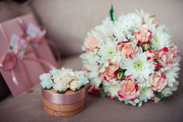 Close-up of a Wedding bouquet of pink roses and white chrysanthemums on a background of pink certificates. a box for rings on a powdery sofa - Photo, Image