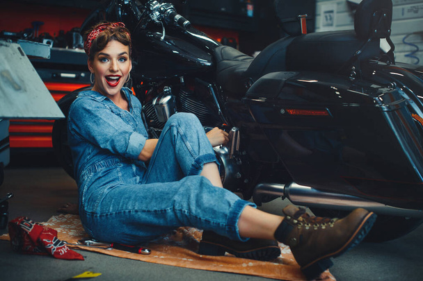 piękna dziewczyna pozowanie naprawy motocykla w warsztacie, pin-up styl, serwis i sprzedaż. - Zdjęcie, obraz