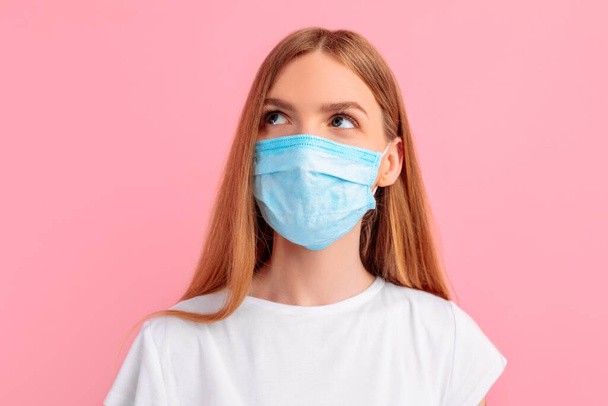 pensive young woman in a medical protective mask on her face, on an isolated pink background. Coronavirus epidemic, quarantine, virus protection - Foto, immagini
