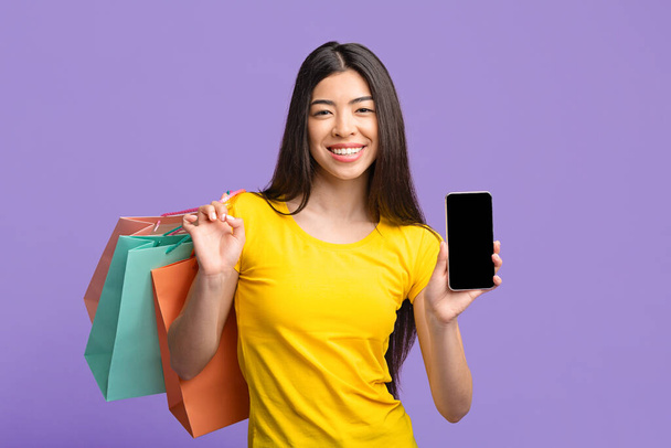 Aplicación de compras. Chica asiática sosteniendo Smartphone con pantalla negra y bolsas de compras
 - Foto, imagen