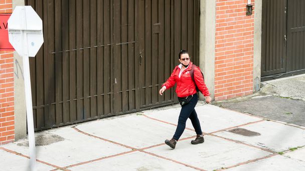 Middle aged woman wearing a mask while walking on the streets of Bogota, Colombia. Red jacket. Avoid the catch and spread of coronavirus.  - Φωτογραφία, εικόνα