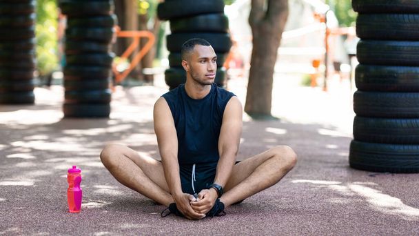 Athletischer schwarzer Kerl dehnt sich auf Asphaltstraße nach seinem morgendlichen Training im Park - Foto, Bild