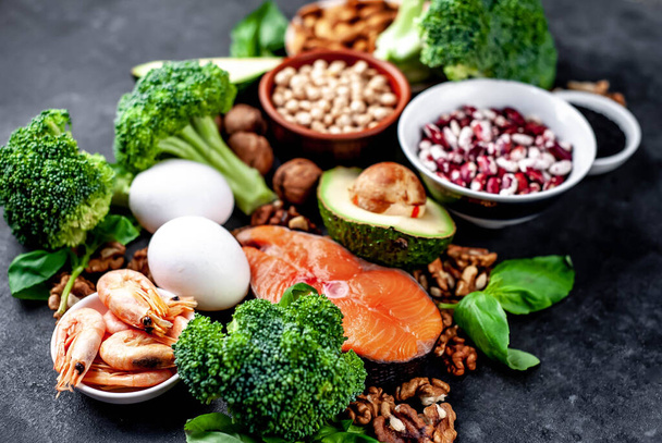 keto dieet met rode zalm, verse groenten en fruit met noten en groenten op zwarte stenen achtergrond - Foto, afbeelding