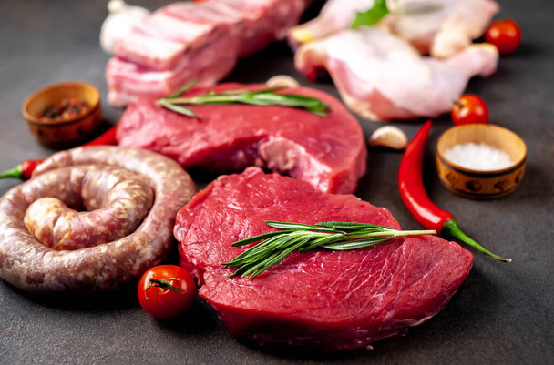 Různé druhy masa. Sortiment čerstvého masa zdobený zeleninou a kořením na černém pozadí - Fotografie, Obrázek