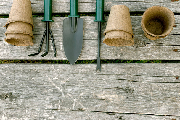 Εργαλεία κήπου και κύπελλα τύρφης για σπορόφυτα σε ξύλινο φόντο. Μια ιδέα εικόνα του εξοπλισμού κήπου με. - Φωτογραφία, εικόνα