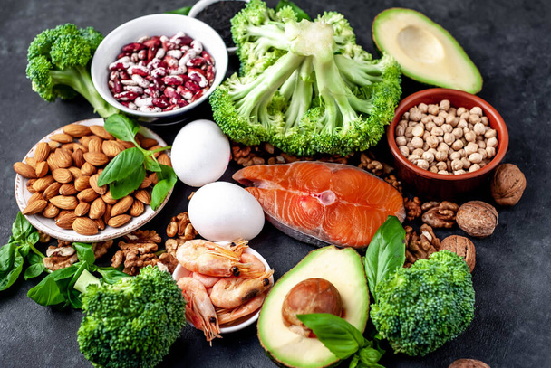 keto diet with red salmon, fresh vegetables and fruits with nuts and greens on black stone background - Photo, Image
