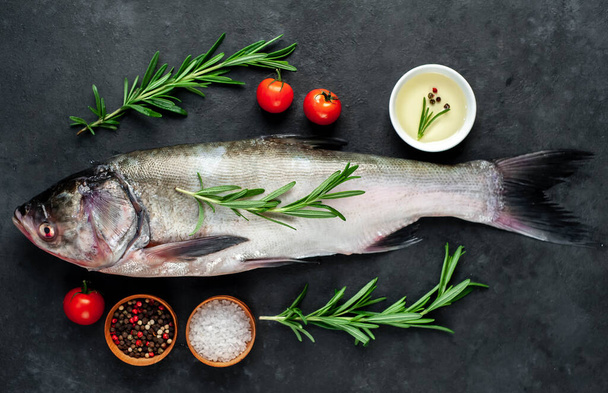 silver carp with sprigs of rosemary, tomatoes, pepper and salt on black background - Photo, Image