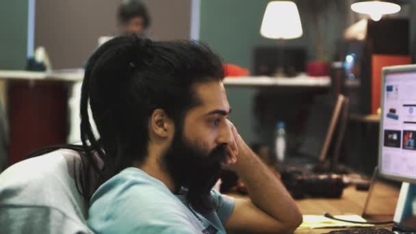 Hombre hindú con rastas y barba se sienta en una computadora en la oficina y trabaja
 - Imágenes, Vídeo