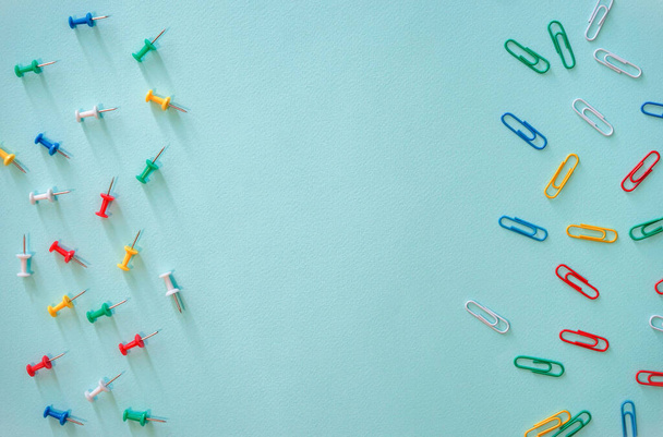 Horizontal close-up flat lay composition of multi-colored paper clips and stationery buttons on a light blue background. Objects of green, red, yellow, white and blue objects. Paper clips in the right - Photo, Image