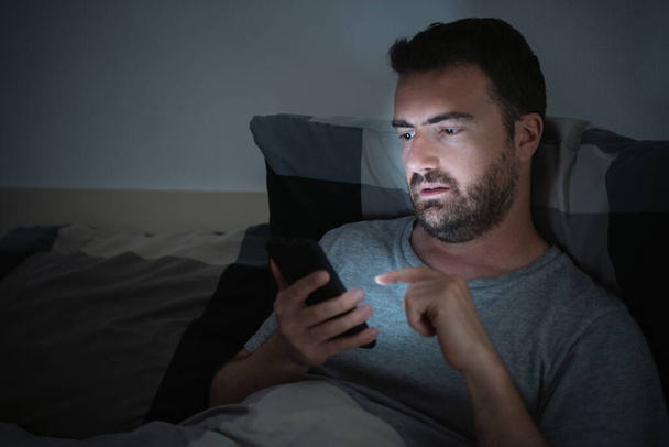 Mies sängyssä katsomassa älypuhelimen näyttöä - Valokuva, kuva