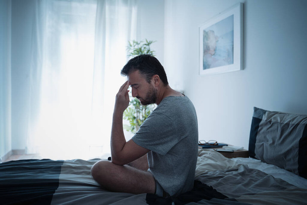 Sad and lonely man seated on his bed - 写真・画像