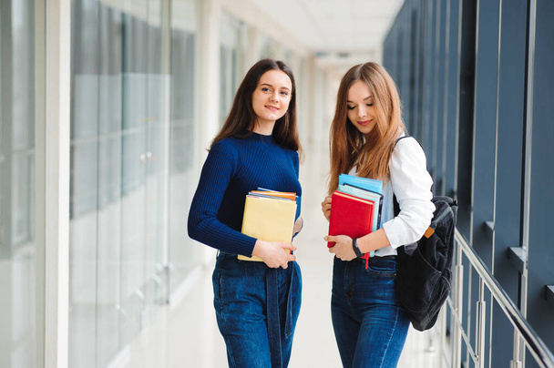 two female students stand in the corridor of the college with books - Zdjęcie, obraz