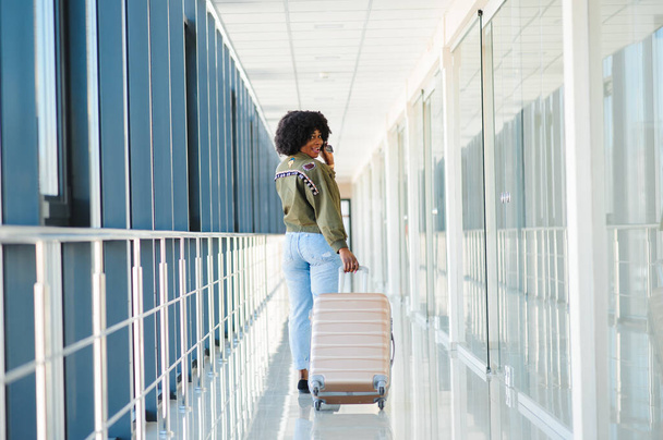 Νεαρή Αφρο-Αμερικανίδα επιβάτης με καθημερινά ρούχα είναι στο αεροδρόμιο με αποσκευές. - Φωτογραφία, εικόνα