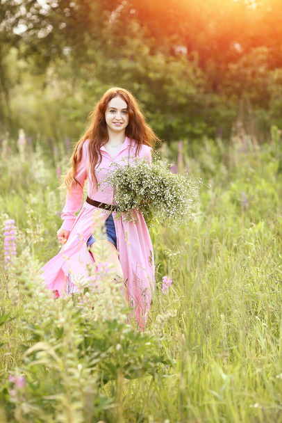 Junge schöne rothaarige Mädchen in einem rosa Kleid mit einem riesigen Strauß Gänseblümchen läuft Sommer im Garten bei Sonnenuntergang. Die Wirkung von Bokeh, Blitz, Sonnenstrahlen. Sommerkonzept. Kopierraum - Foto, Bild