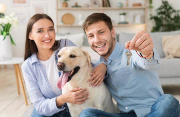 Νεαρό ευτυχισμένο ζευγάρι με σκύλο που δείχνει τα κλειδιά από το νέο σπίτι - Φωτογραφία, εικόνα