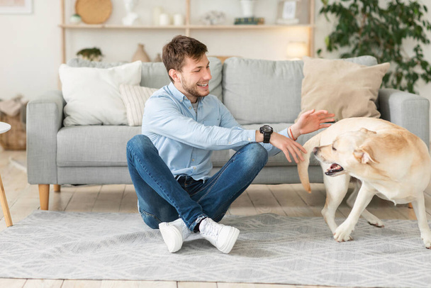 Красивый мужчина играет со своей собакой в гостиной
 - Фото, изображение