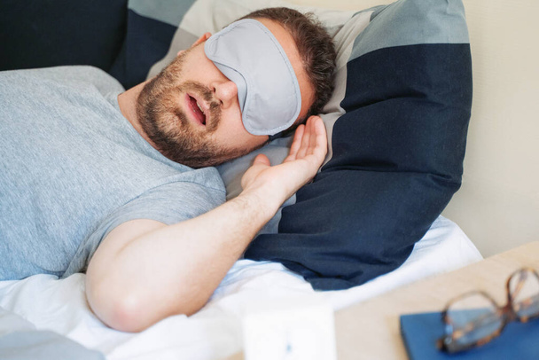 Man portrait in bed wearing sleeping eye mask feeling comfortable - Foto, Imagem