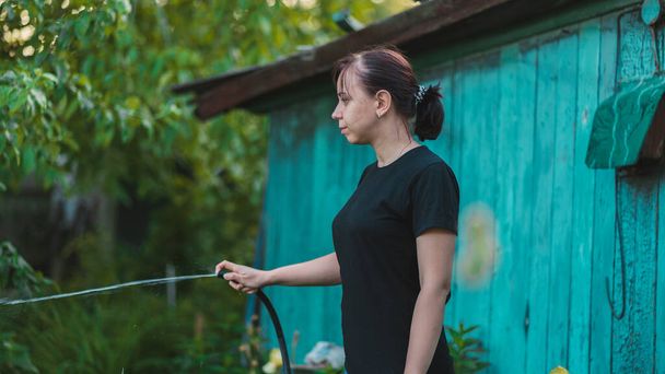 Woman watering the garden from hose. Female spraying water on vegetables with a garden hose. A happy woman with a hose takes care of the garden. - Foto, Imagem