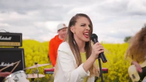 A musical group plays in a field of yellow flowers. The soloist sings into the microphone. Energetic music and dancing. Play musical instruments - Footage, Video