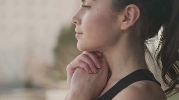 Klidná mladá žena v černé teplákové soupravě stojí u okna v šedém studiu - Záběry, video
