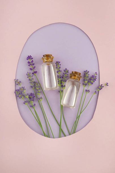 Huile essentielle de lavande en bouteille de verre et fleurs de lavande sur fond rose et violet - Photo, image