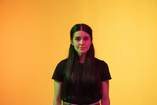 Caucasian young womans portrait on yellow background in neon light - Foto, Imagen