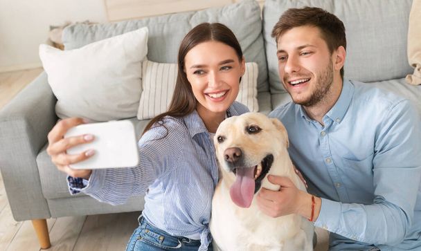 Jeune couple prenant autoportrait avec chien à la maison - Photo, image