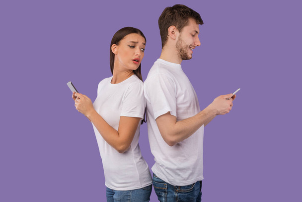 Porträt eines jungen Paares, das mit dem Handy Rücken an Rücken steht - Foto, Bild