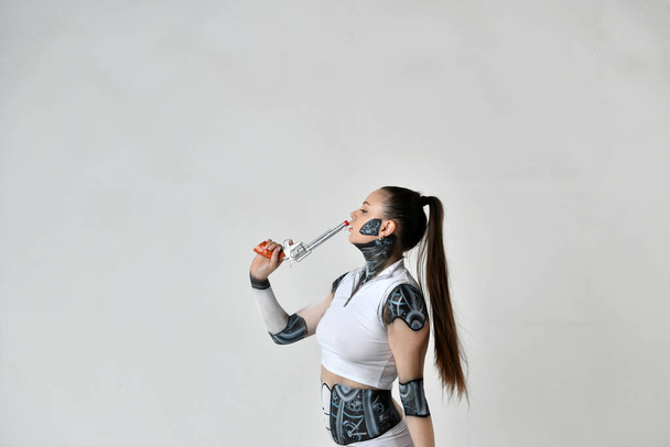 όμορφο κορίτσι με ρούχα ρομπότ ποζάρουν με ασημένια περίστροφα - Φωτογραφία, εικόνα