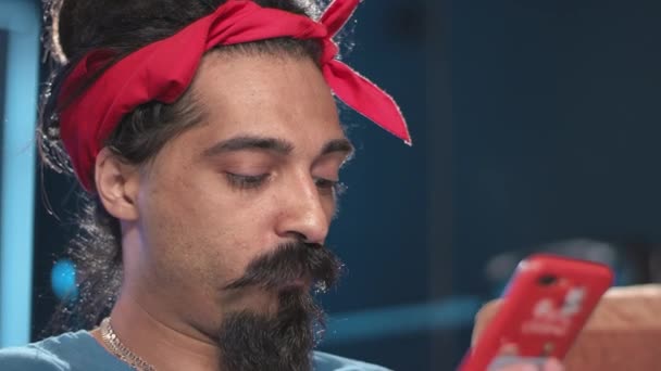 L'hindou avec des dreads, des moustaches, une longue barbe et un mouchoir rouge sur la tête joue à des jeux sur un smartphone et compose un message. - Séquence, vidéo