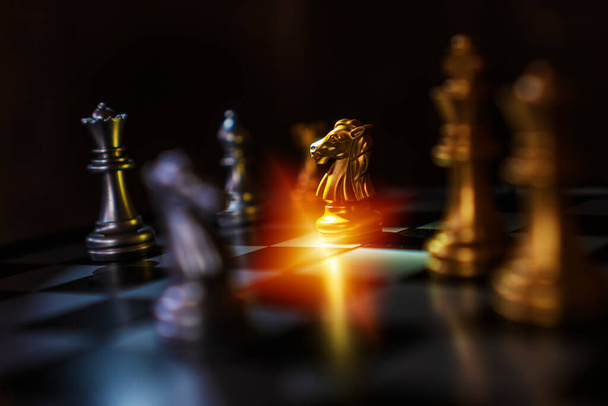 Peça de cavalo de xadrez dourado no jogo de tabuleiro de xadrez com xadrez adversário em fundo preto com efeito de luz para ideias e competição e estratégia. Líder de negócios bem sucedido, conceito corajoso ou destemido
. - Foto, Imagem