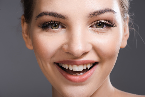 close-up van gelukkig jong vrouw met make-up glimlachen en kijken naar camera geïsoleerd op grijs - Foto, afbeelding