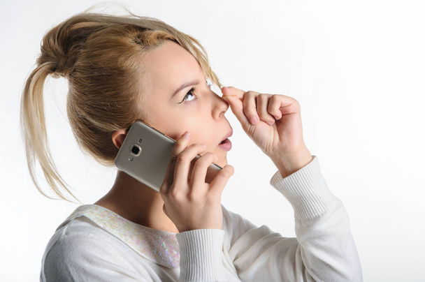 lateral view of a 20-years blond girl in white blouse and blue skirt on white background talking on the cell phone - Foto, Imagen