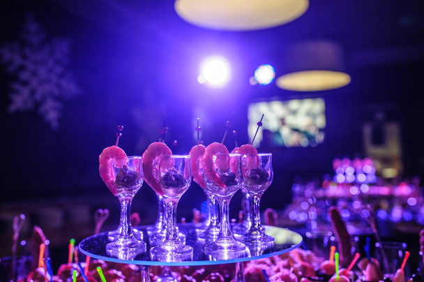 Mesa buffet con aperitivos, canapés; camarones con salsa en vasos en una fiesta de cumpleaños con luces azules
 - Foto, Imagen