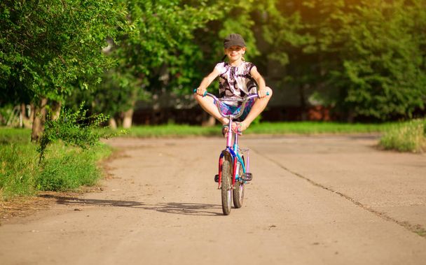 木の背景とキャップに乗る自転車で小さな面白い女の子。インターネットや電子機器のない子供時代 - 写真・画像