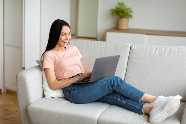 Mujer en el ordenador portátil haciendo videollamada sentada en el sofá en interiores
 - Foto, imagen