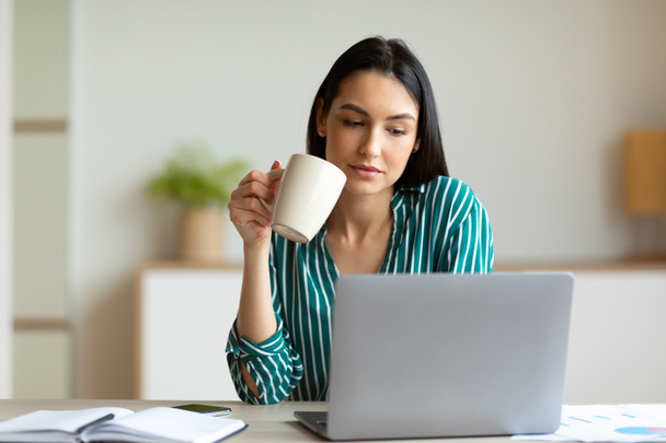 Ofis kızı laptopta kahve içiyor, iş yerinde oturuyor. - Fotoğraf, Görsel