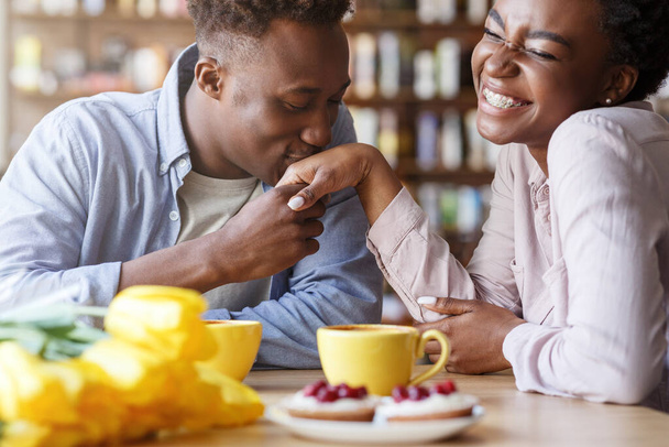 Handsome African American guy kissing his girlfriends hand at coffee shop - Foto, imagen