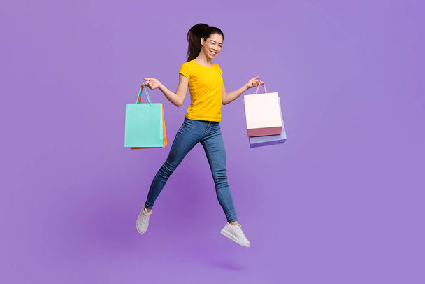 Счастливого шоппинга. Радостная азиатская девочка прыгает в воздухе с огромными сумками для покупок
 - Фото, изображение