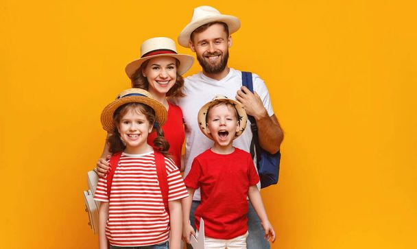 Begeisterte Eltern und Kinder mit Sommermützen lächeln und schauen in die Kamera, während sie vor gelbem Hintergrund in den Urlaub fahren. - Foto, Bild