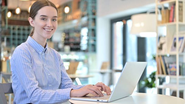 Ноутбук использования молодая женщина улыбаясь на камеру в кафе
 - Фото, изображение