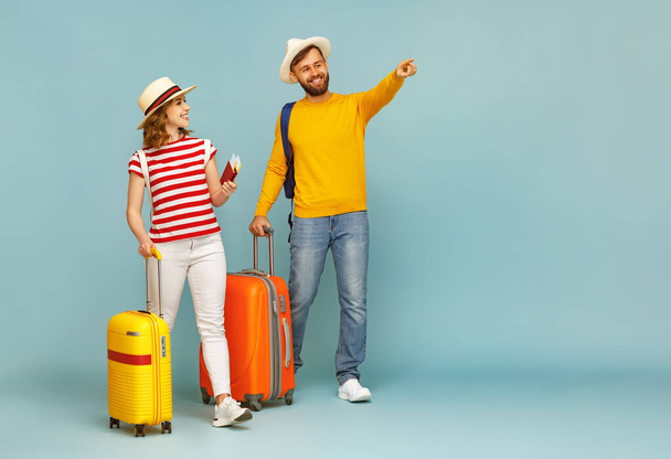 Full body cheerful bearded man pointing away for smiling girlfriend with luggage and tickets during summer vacation against blue backdro - Photo, Image