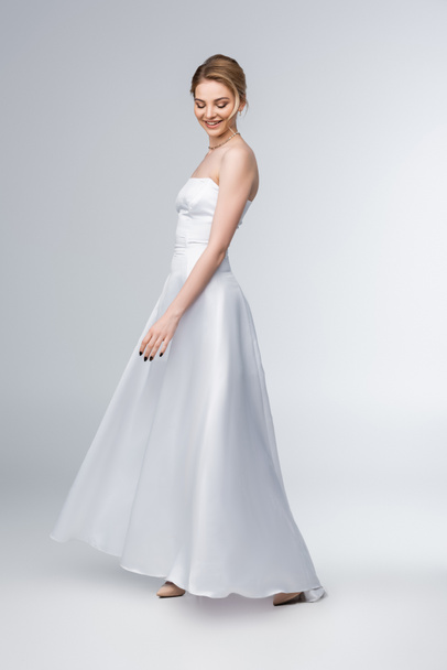 smiling bride in elegant wedding dress standing on grey  - Valokuva, kuva