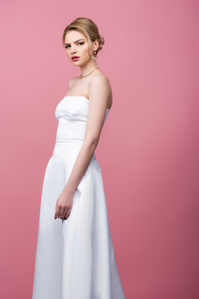 serious bride in white wedding dress looking at camera isolated on pink  - Photo, Image