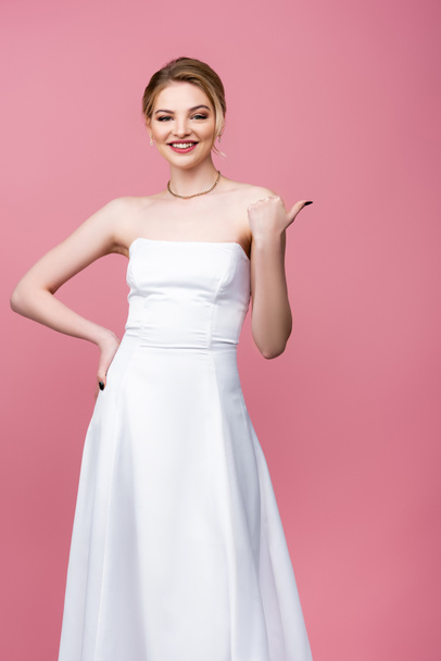 happy bride in white wedding dress pointing with thumb isolated on pink  - Fotoğraf, Görsel
