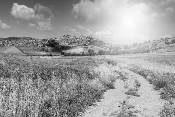Eine mittelalterliche Stadt in den sizilianischen Bergen. Sizilianische Landschaft bei Sonnenaufgang, Hügel, Felder, Blumen, Weiden und Sonnenlicht. Schwarz-Weiß-Bild - Foto, Bild