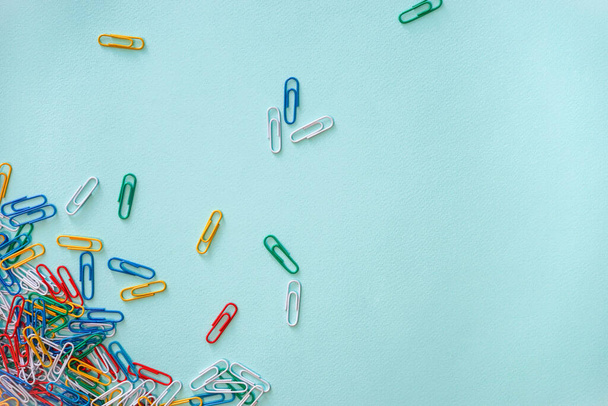 Horizontal close-up flat lay composition of multi-colored paper clips on a light blue background. A pile of green, red, yellow, white and blue objects in the lower left corner. Part of the paper clips - Fotoğraf, Görsel