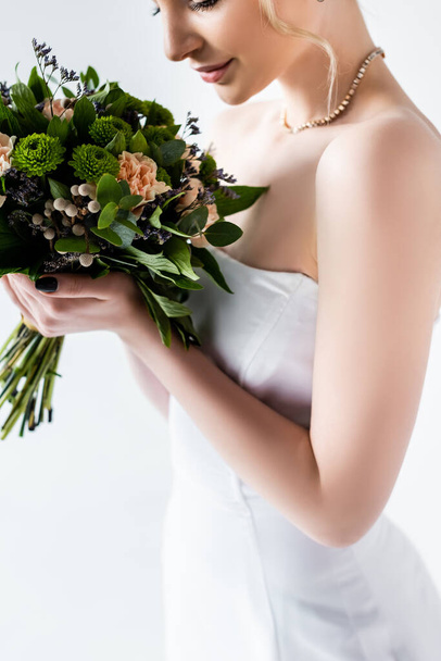 cropped view of bride in elegant wedding dress holding flowers isolated on white  - Fotó, kép